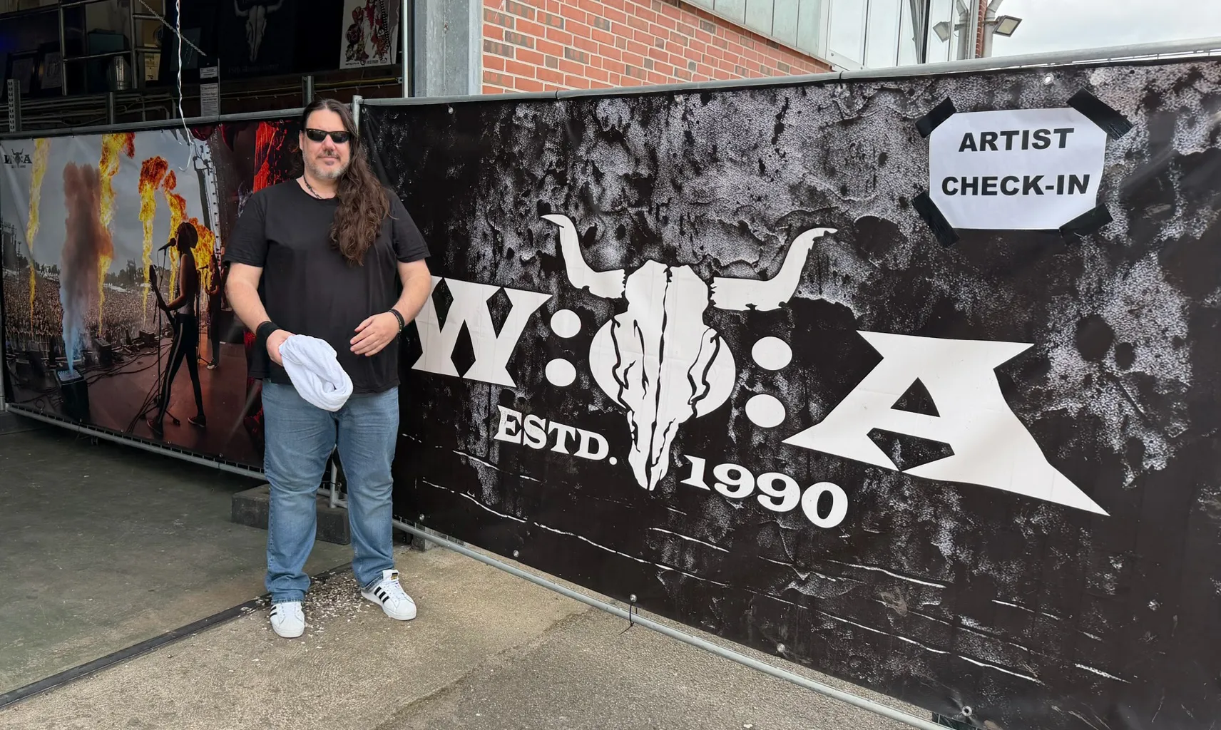 Maxim Matthew steht vor dem Banner des Artist Check-in mit dem W:O:A-Logo und der Zeile „Estd. 1990“.