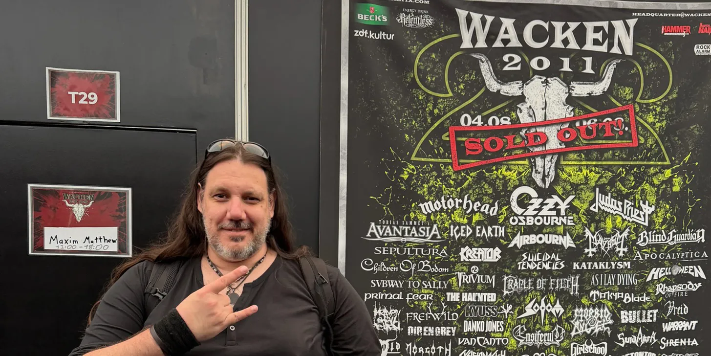 Maxim Matthew zeigt die Pommesgabel neben seiner Garderobentür, an der sein Name steht. Daneben hängt das Wacken-Plakat von 2011 mit Ozzy Osbourne in der ersten Reihe.