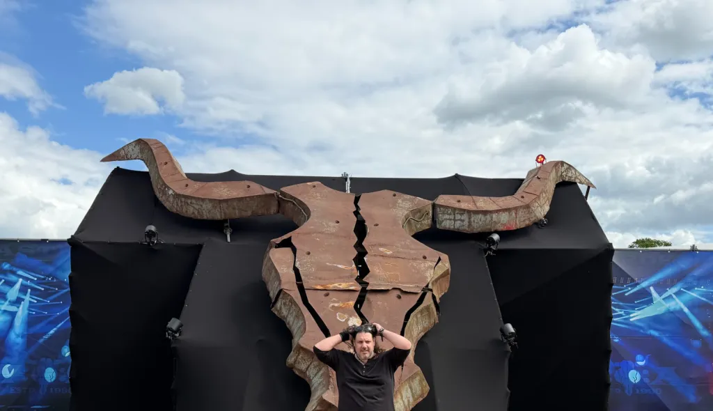 Maxim Matthew steht mit ausgebreiteten Armen vor dem riesigen Stierschädel auf dem Festivalgelände.
